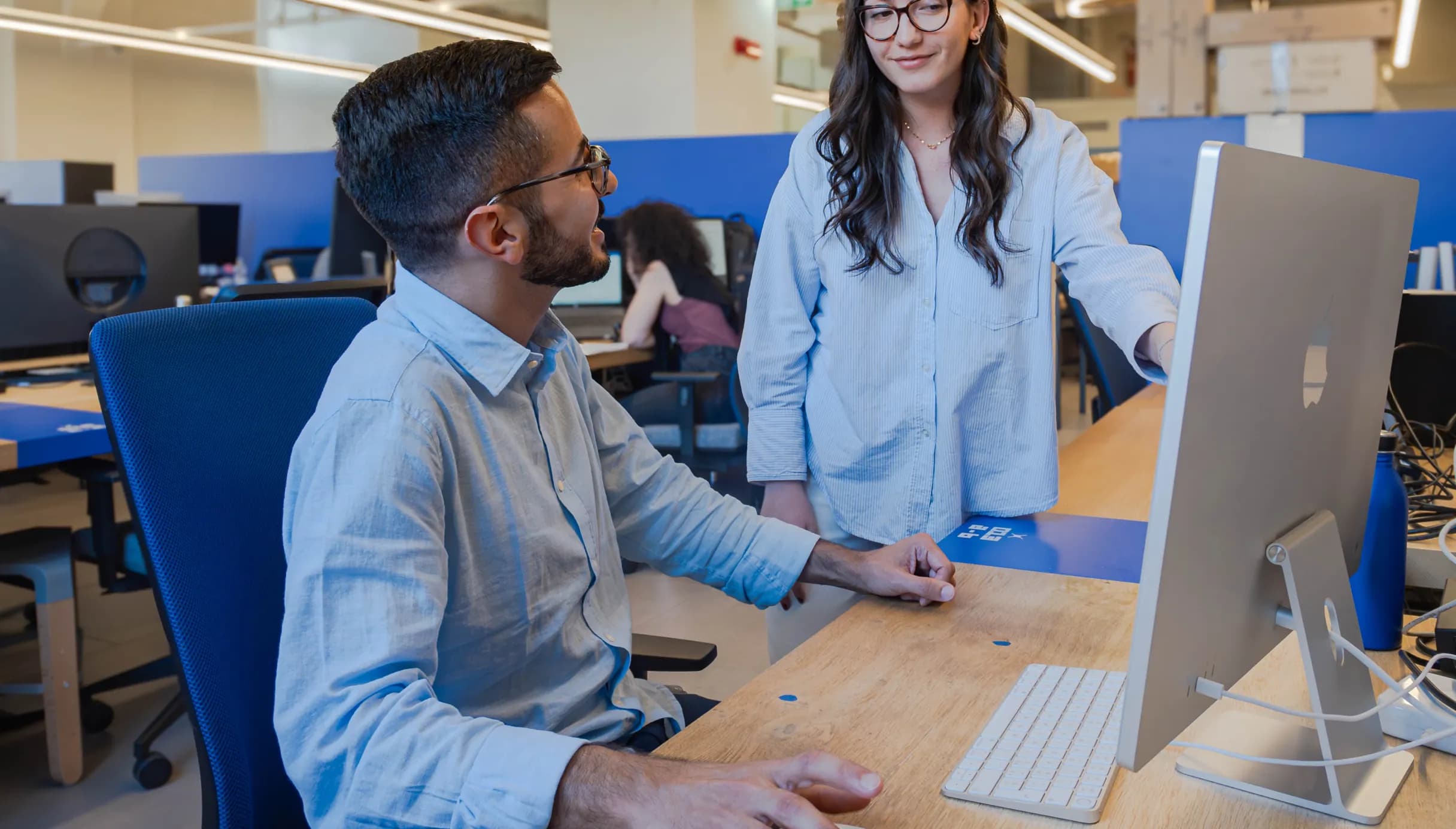 Due professionisti discutono davanti a un iMac all’interno degli spazi di coworking di Nana Bianca a Firenze, in un ambiente moderno e attrezzato per startup e freelance.