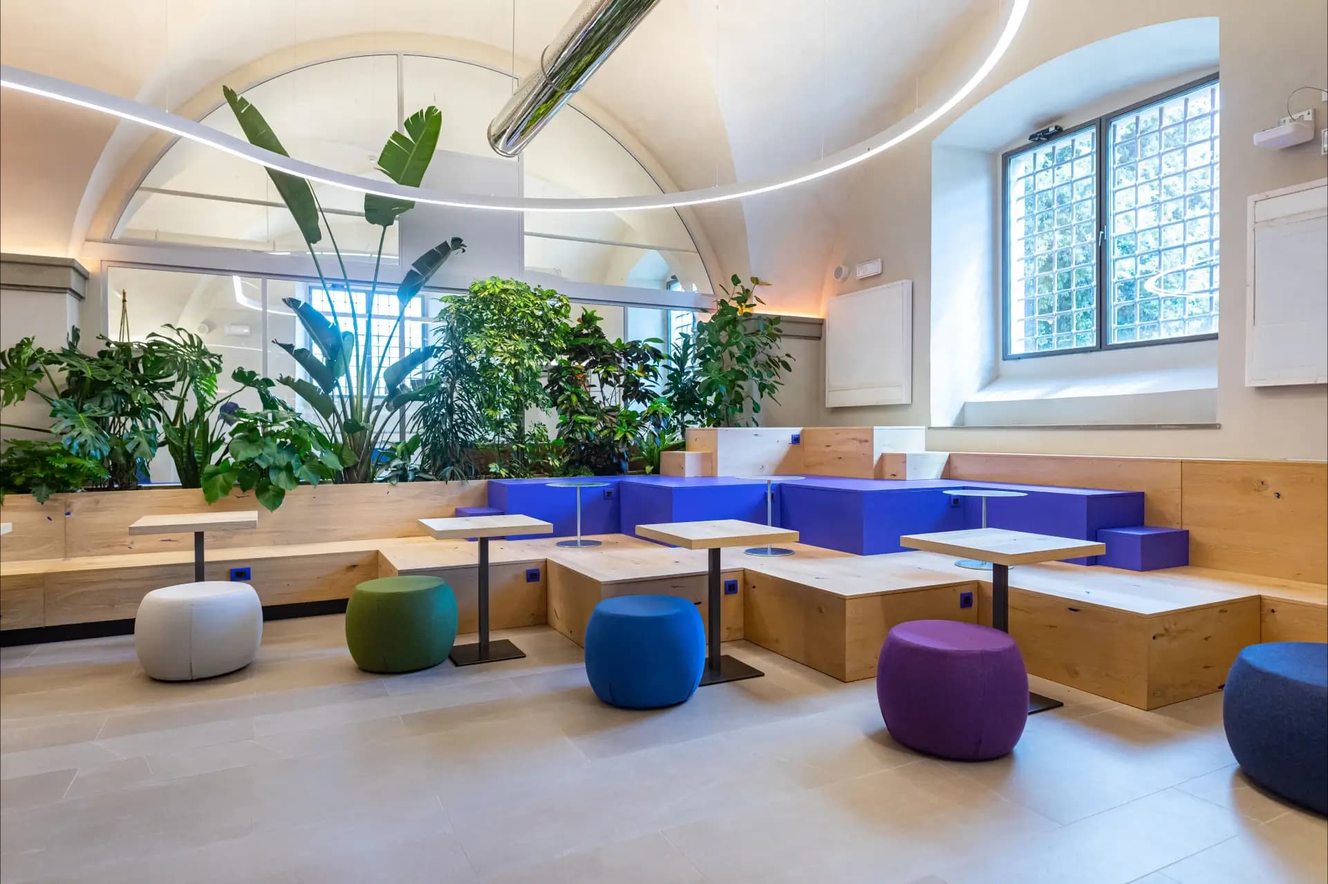 Spazio di coworking e relax di Nana Bianca a Firenze, con design moderno, arredi in legno, sedute colorate e piante verdi. Un ambiente ideale per lavorare in un coworking innovativo nel cuore dell'Innovation Center.