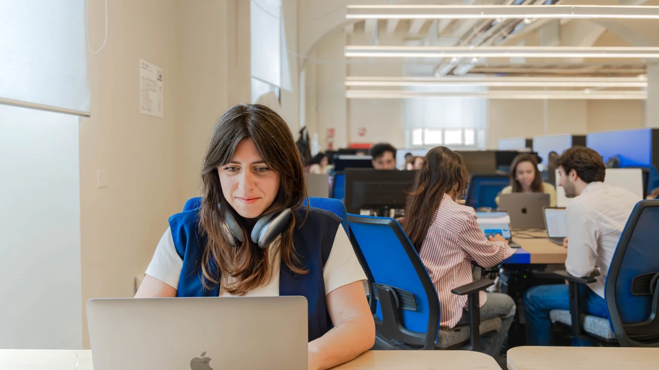 Una donna che lavora al suo laptop in uno spazio di coworking moderno presso Nana Bianca a Firenze, circondata da altri professionisti che collaborano in un ambiente di ufficio condiviso. Lo spazio è progettato per la produttività e il lavoro di squadra, con un layout open space e sedute confortevoli.