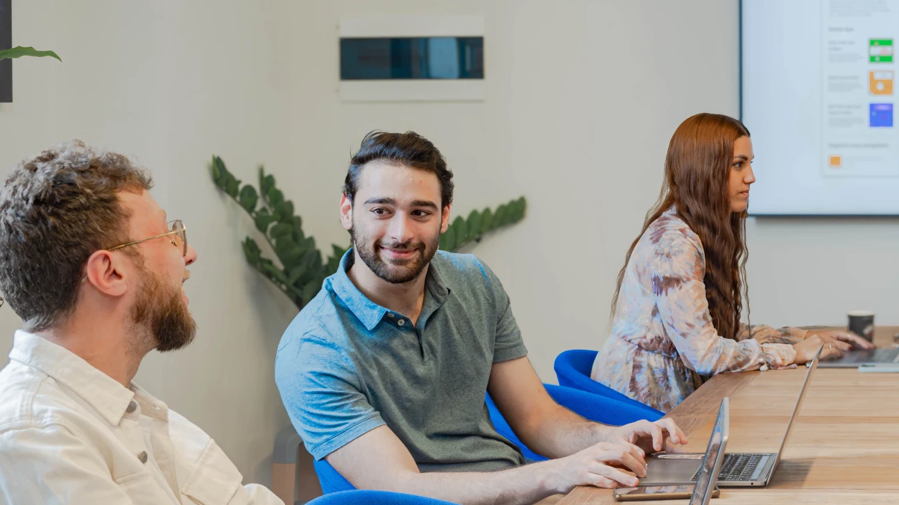 Tre colleghi impegnati in una discussione durante una riunione presso Nana Bianca a Firenze. L'ambiente di ufficio condiviso presenta una moderna sala riunioni, ideale per il coworking e la collaborazione, con laptop e strumenti digitali in uso.